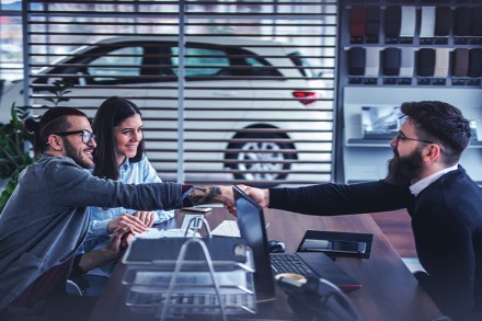 two car buyers shaking hands with dealer while closing a car deal