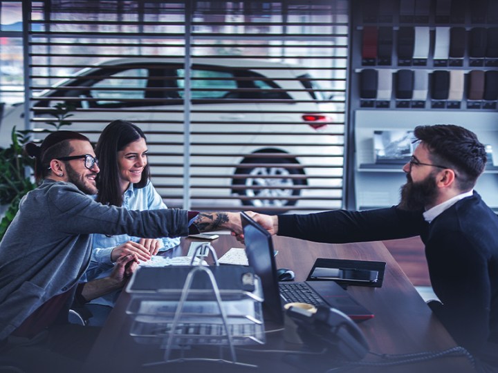 two car buyers shaking hands with dealer while closing a car deal